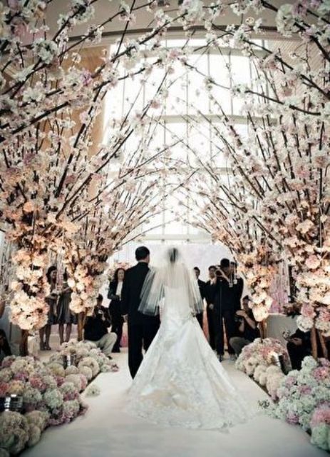 a dreamy blooming wedding ceremony space decorated completely with cheery blossom branches and lined up with their arrangements, too