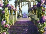 a bold wedding ceremony space fully done with lilac, purple hydrangeas and greenery, with pillars interwoven with them and petals on the ground
