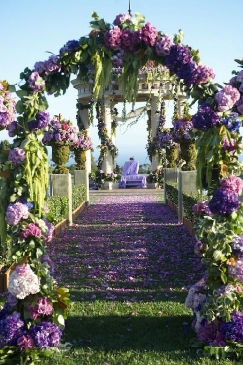 a bold wedding ceremony space fully done with lilac, purple hydrangeas and greenery, with pillars interwoven with them and petals on the ground