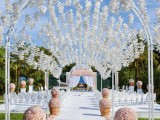a dreamy wedding ceremony space with white orchids forming a roof and lots of blush blooms lining up the aisle
