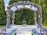 a beautiful wedding arbor covered with white and blue hydrangeas, the same blooms lining up the aisle and making it wow