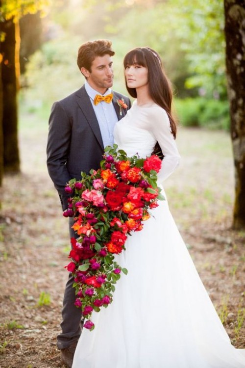a super bold and oversized cascading wedding bouquet of pink, red and orange blooms and greenery is a bold statement for your wedding