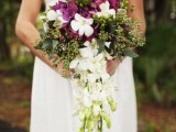 a catchy tropical cascading wedding bouquet with white and purple orchids, greenery and blooming and greenery cascading parts is a lovely idea for a modern tropical wedding