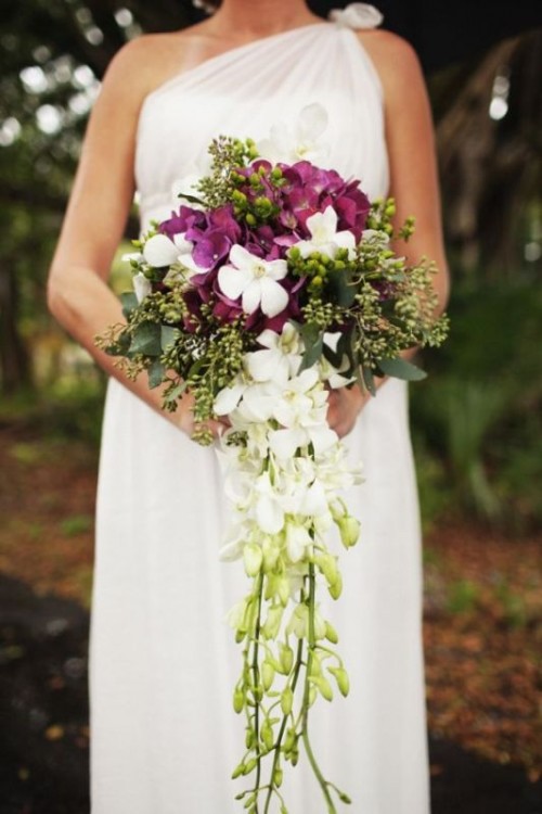 a catchy tropical cascading wedding bouquet with white and purple orchids, greenery and blooming and greenery cascading parts is a lovely idea for a modern tropical wedding