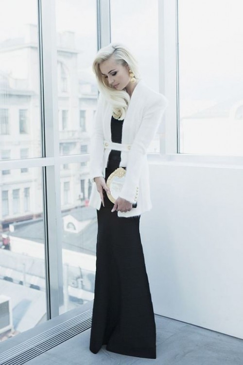 a black fitting maxi dress, a creamy blazer with straps and long sleeves and a white clutch