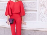 a red jumpsuit with a bateau neckline, long sleeves, silver heels, a purple clutch and statement earrings