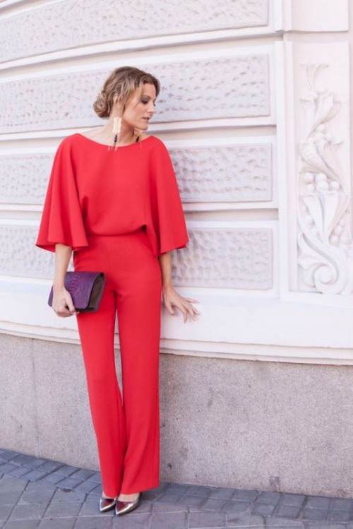 a red jumpsuit with a bateau neckline, long sleeves, silver heels, a purple clutch and statement earrings