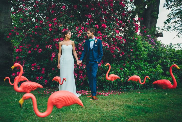 Wedding portraits taken in a garden, with purple and fuchsia blooms and flamingo decor on the lawn for a whimsy and playful touch