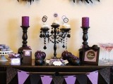 a purple and black Halloween sweets table with purple candles and a bunting, feathers, pumpkins and crystals is a refined and cool idea