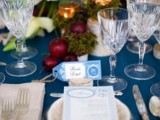 a blue winter wedding tablescape with red and white blooms, apples, blue cards and neutral napkins and menus