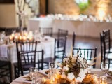 a rustic winter table in neutrals, with candles in jars, white napkins, a winter centerpiece of cotton, wheat, dried blooms