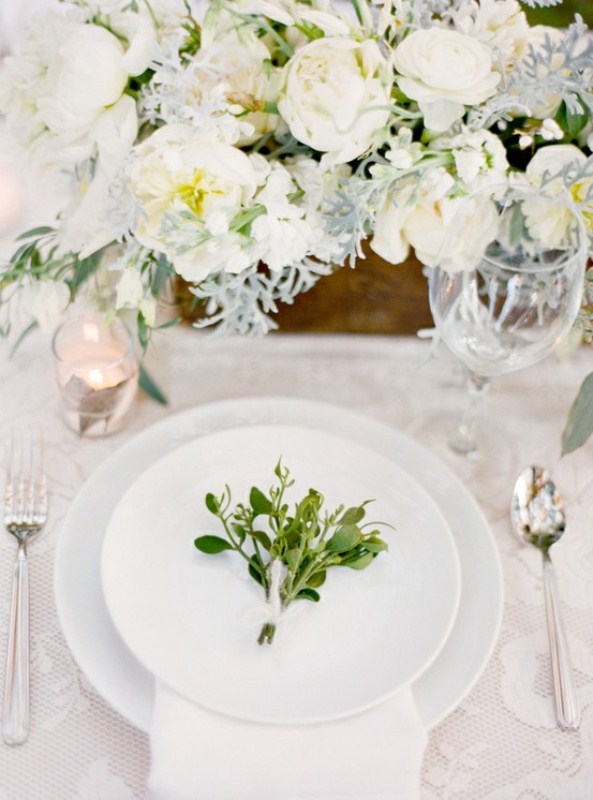a white winter tablescape with white blooms, pale miller, mercury glass candleholders and greenery on each place setting