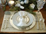 an elegant winter tablescape with note paper, Christmas ornaments, evergreens, shiny snowflakes and candleholders
