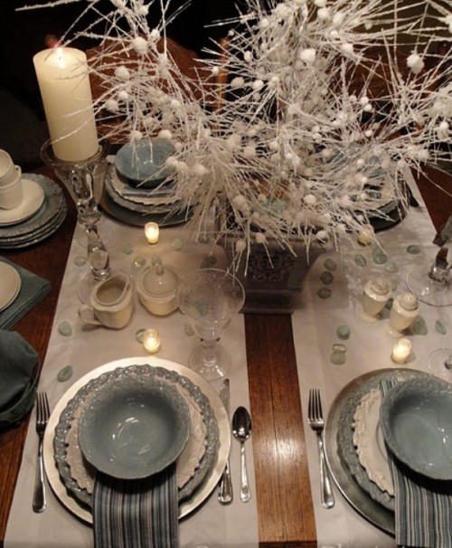 a grey and white winter wedding tablescape with grey and white porcelain, pebbles, candles, bead arrangement in a vase