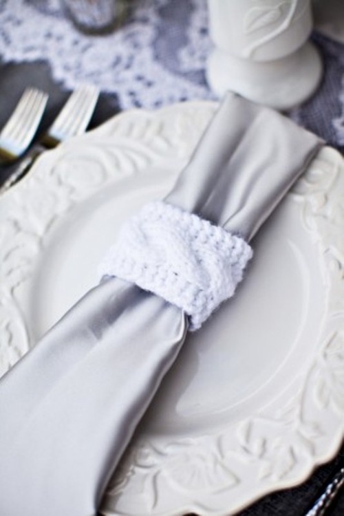 a silver and white tablescape with white porcelain with a silver napkin with knit napkin rings, lace runners
