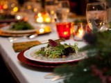 a green and red winter wedding table with lots of lights and candles in candleholders, evergreens and silver cutlery