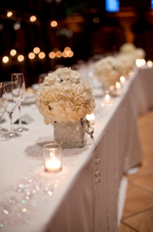 a frozen winter wedding tablescape with crystals, white blooms, a sparkling white tablecloth and shiny vases