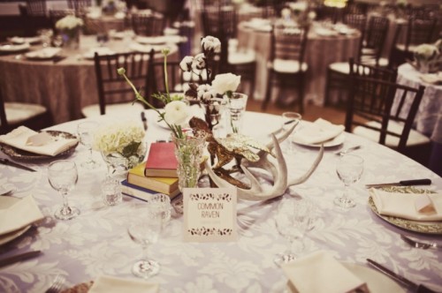 a winter wedding tablescape with books, antlers, cotton branches, some white blooms in glasses