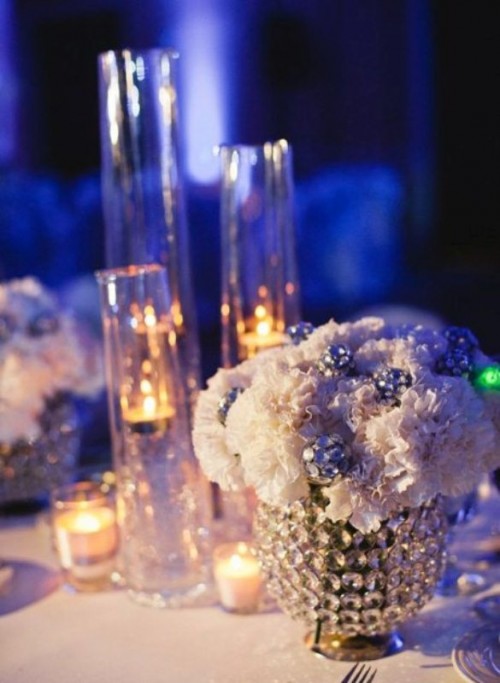 white blooms with crystals in a shiny vase, candles in vases and lots of shiny elements for a glam winter wedding table