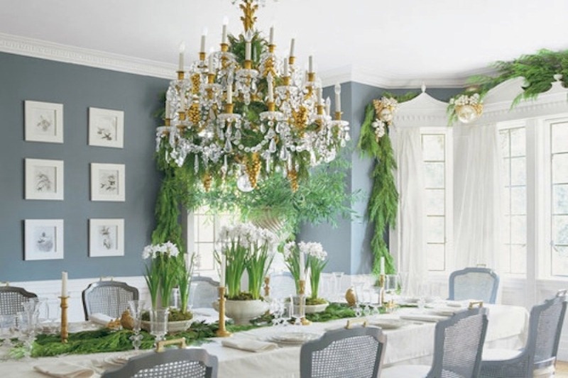 a winter wedding tablescape done with lots of evergreens, candles, blooms in pots, a large crystal chandelier with candles