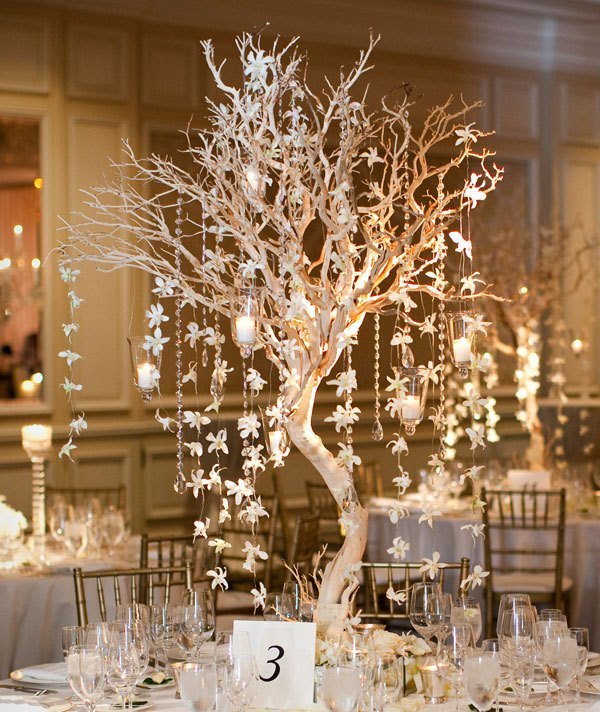 a white winter wedding table with a tree centerpiece with hanging crystals and candles, a neutral table number and porcelain