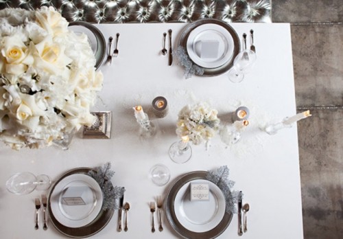 an elegant neutral winter wedding tablescape with neutral blooms, candles, sivler cutlery and chargers, frozen snowflakes and foliage