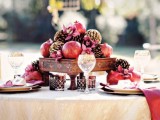 a winter wedding tablescape with red glasses, napkins, pomegranates and pinecones and red napkins