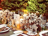 a rustic winter wedding tablescape with a burlap runner, cotton centerpieces, brown pockets, candles and simple cutlery