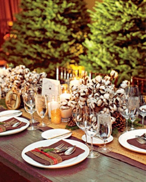 a rustic winter wedding tablescape with a burlap runner, cotton centerpieces, brown pockets, candles and simple cutlery