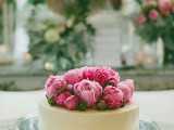 a white chocolate covered wedding cheesecake topped with fresh pink peonies
