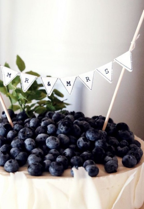 a classic cheesecake decorated with white chocolate petals and lots of blueberries on top plus a banner
